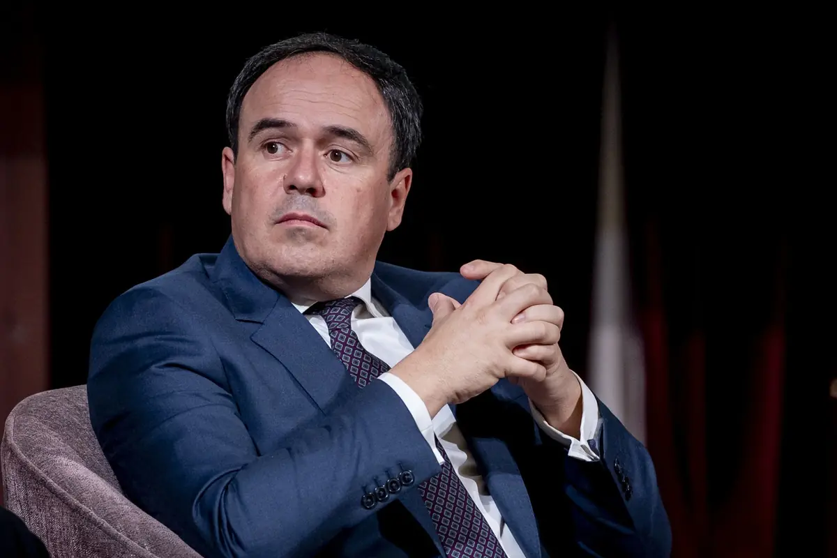 Hombre de mediana edad con traje azul y corbata sentado en un sillón mirando hacia un lado con las manos entrelazadas