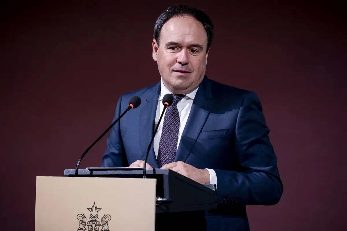 Hombre con traje azul hablando en un atril con dos micrófonos frente a un fondo oscuro