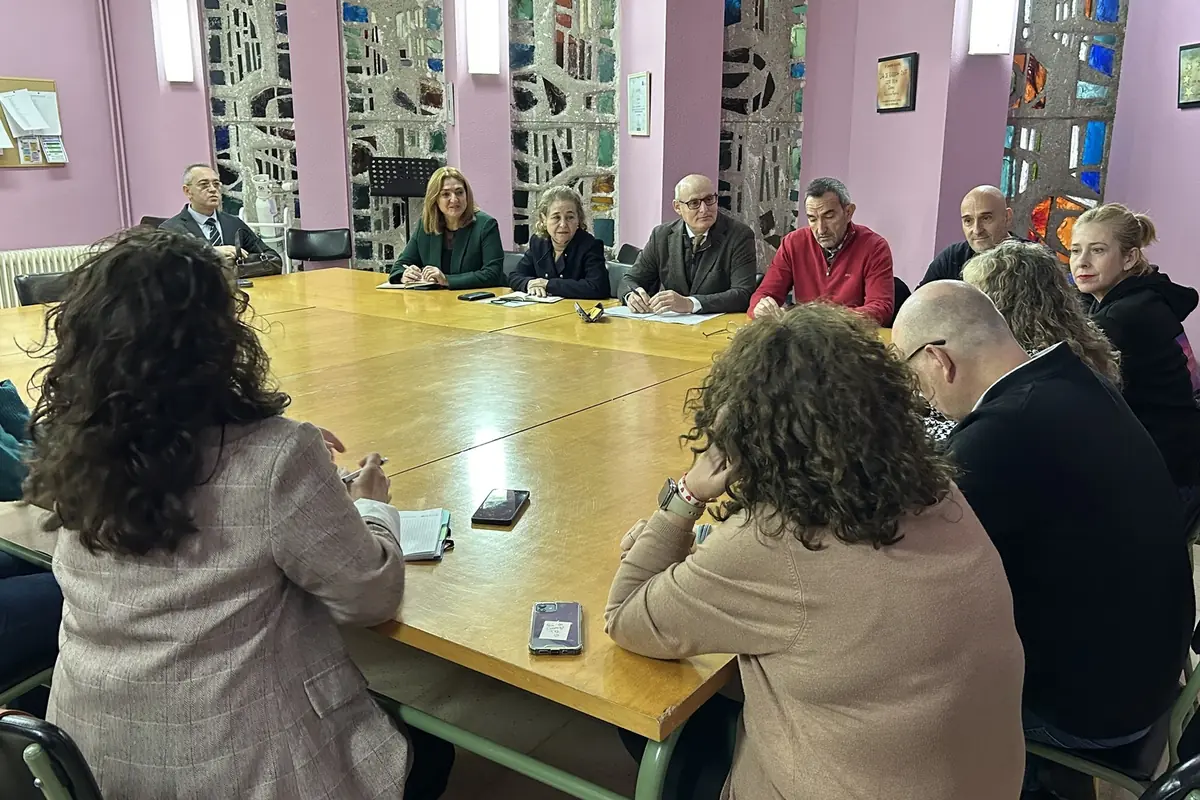 Reunión de varias personas sentadas alrededor de una gran mesa de madera en una sala con paredes rosas y vitrales de colores mientras toman notas y conversan