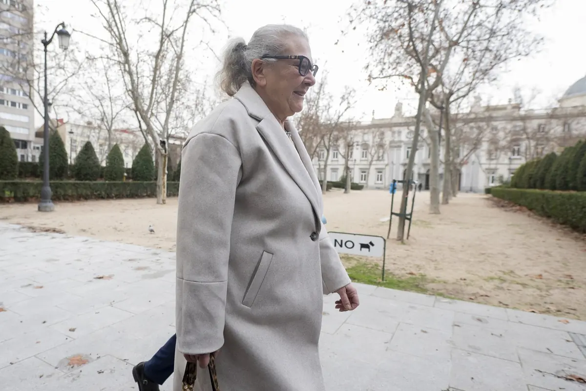 Mujer mayor con abrigo claro y gafas de sol caminando por un parque urbano en invierno