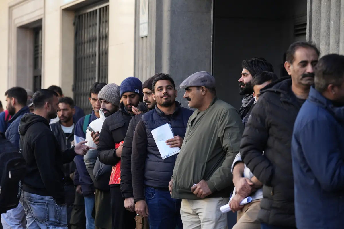 Grupo de hombres haciendo fila en la calle frente a un edificio oficial con documentos en la mano