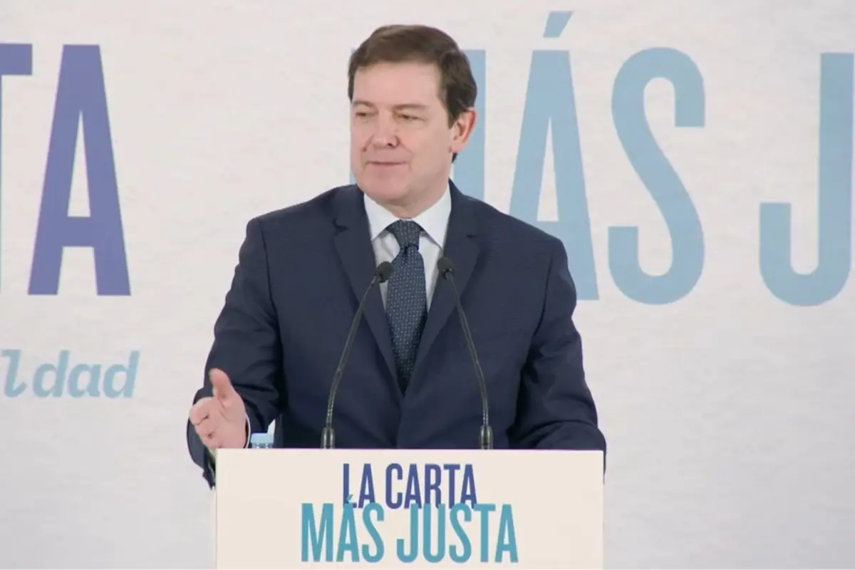 Hombre con traje azul hablando en un atril con dos micrófonos y el lema La carta más justa impreso en el frente