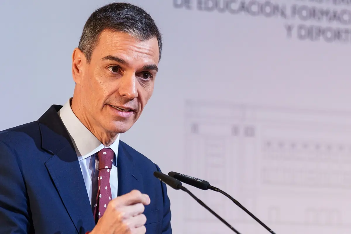 Hombre con traje azul y corbata roja hablando frente a un micrófono en un acto público