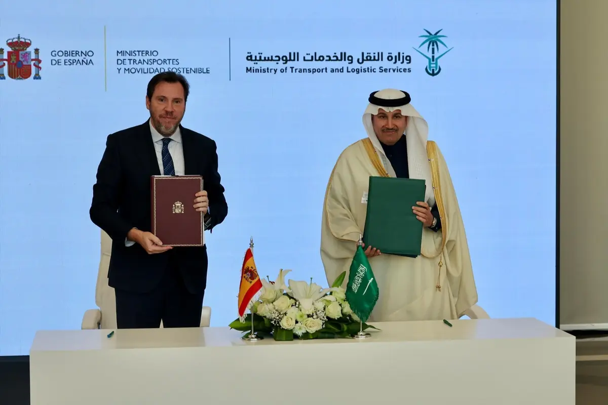 Representantes de España y Arabia Saudí posan con carpetas oficiales tras firmar un acuerdo de transporte y servicios logísticos en una mesa con banderas y flores