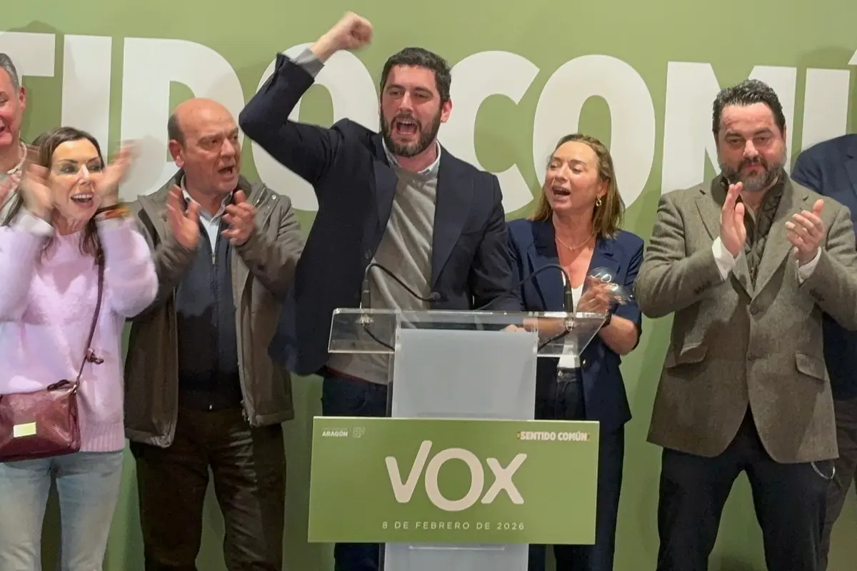 Grupo de personas en un mitin de VOX aplaudiendo y celebrando mientras un hombre en el centro levanta el puño y habla desde un atril con el logo del partido