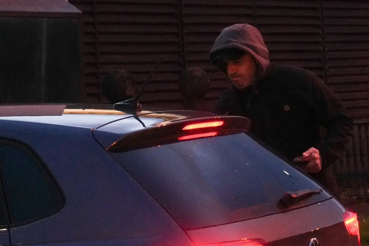 Hombre con sudadera y gorra manipulando la puerta trasera de un coche estacionado al anochecer