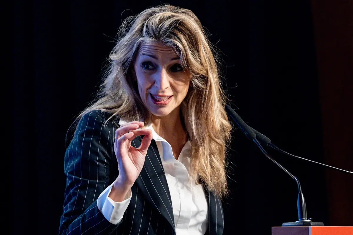 Mujer con traje de rayas hablando en un atril y gesticulando con la mano frente a un micrófono