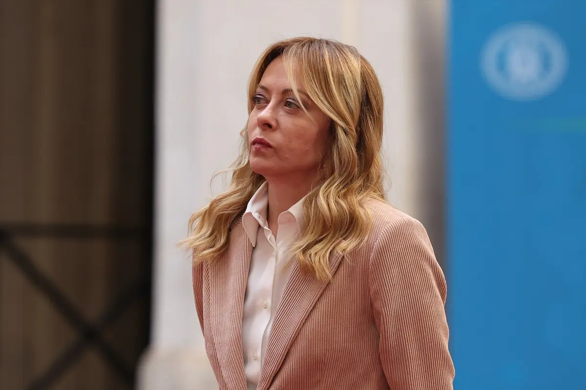 Mujer rubia con chaqueta rosa claro y camisa blanca mirando seria hacia un lado en un entorno urbano