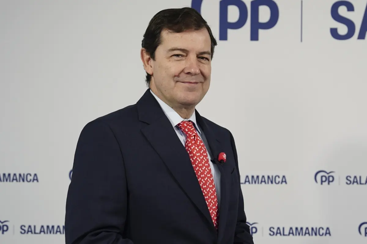 Hombre de mediana edad con traje oscuro y corbata roja posando sonriente frente a un fondo con el logotipo del PP y la palabra Salamanca Hombre de mediana edad con traje oscuro y corbata roja posando sonriente frente a un fondo con el logotipo del PP y la palabra Salamanca