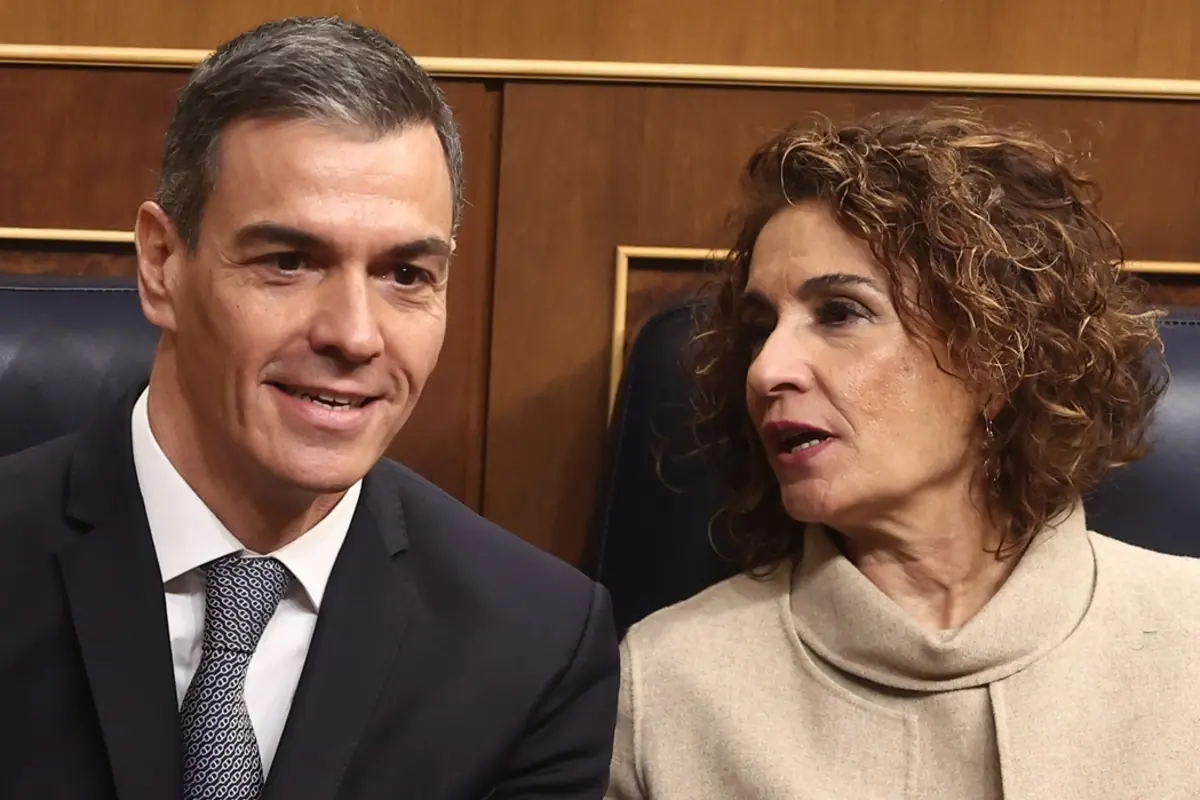 Dos personas sentadas en un escaño parlamentario conversan de cerca mientras miran hacia direcciones opuestas Dos personas sentadas en un escaño parlamentario conversan de cerca mientras miran hacia direcciones opuestas