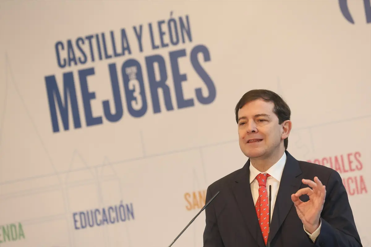 Hombre con traje y corbata roja hablando en un atril frente a un cartel con el lema Castilla y León Mejores