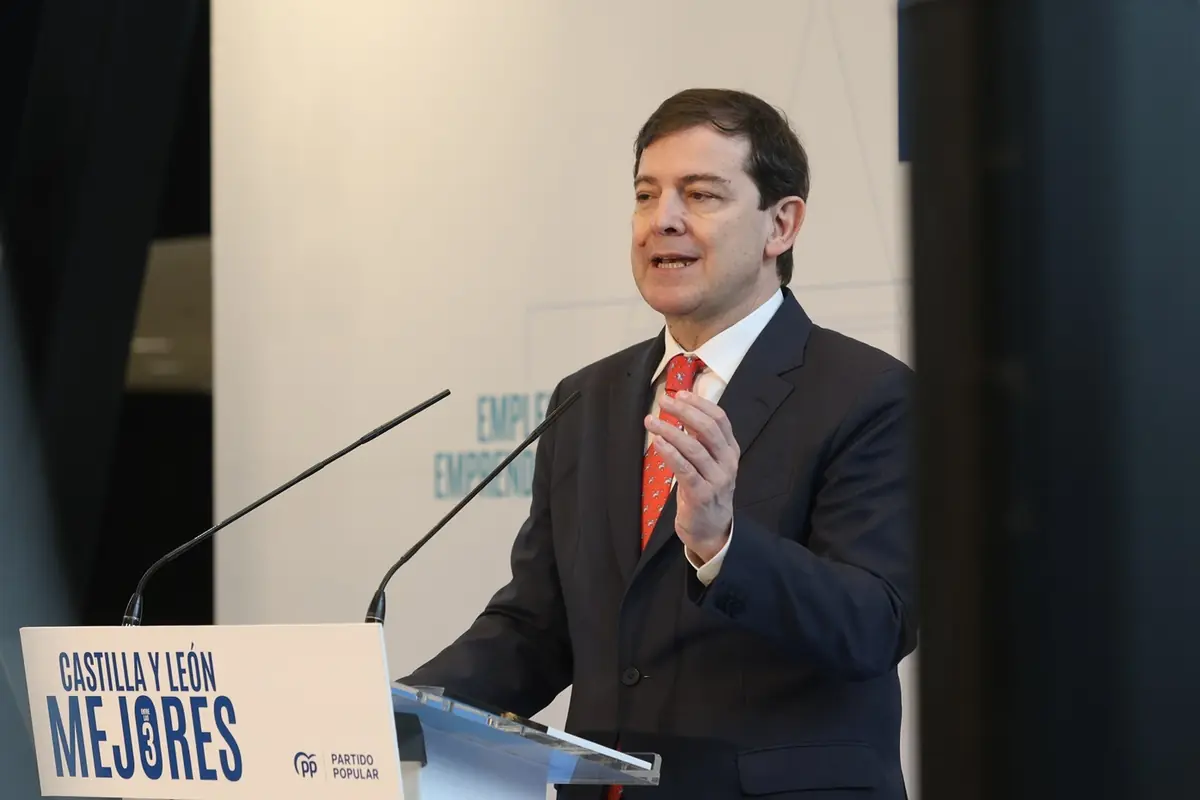Hombre con traje oscuro y corbata roja hablando frente a dos micrófonos en un acto público