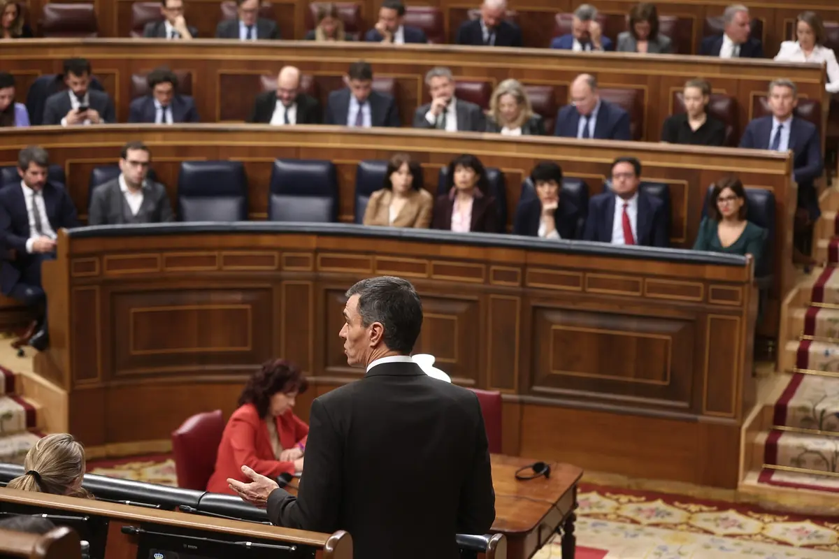 Hombre de traje hablando desde el atril en un parlamento mientras los diputados escuchan desde sus escaños