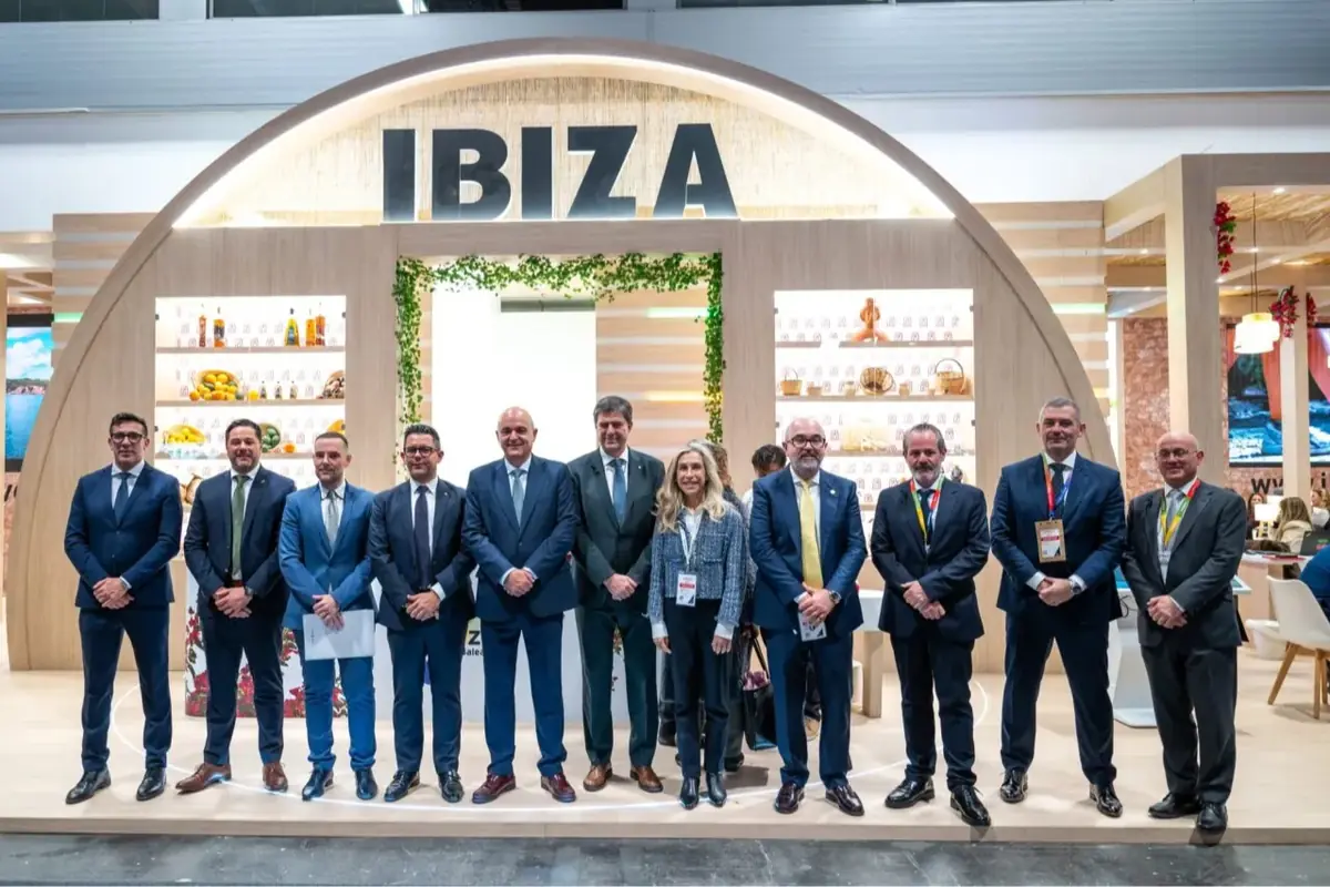 Grupo de representantes posando de pie con trajes formales frente a un stand promocional de Ibiza en una feria turística