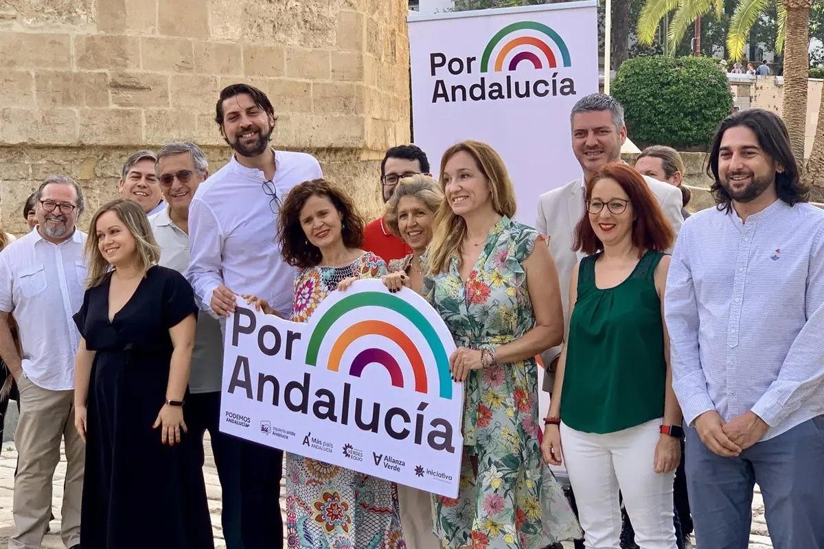 Grupo de personas sonriendo al aire libre sosteniendo un cartel y un fondo con el lema Por Andalucía y un logotipo de arcoíris