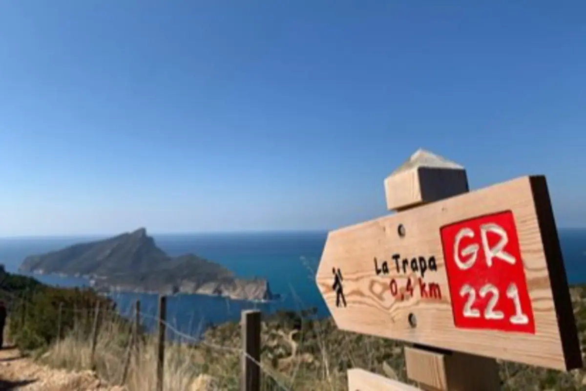 Cartel de madera del sendero GR 221 hacia La Trapa con vistas a un acantilado y al mar Mediterráneo al fondo