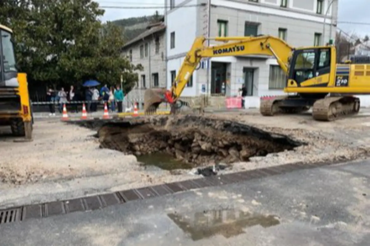 Excavadora trabajando en una calle con un gran socavón rodeado de conos y curiosos al fondo Excavadora trabajando en una calle con un gran socavón rodeado de conos y curiosos al fondo