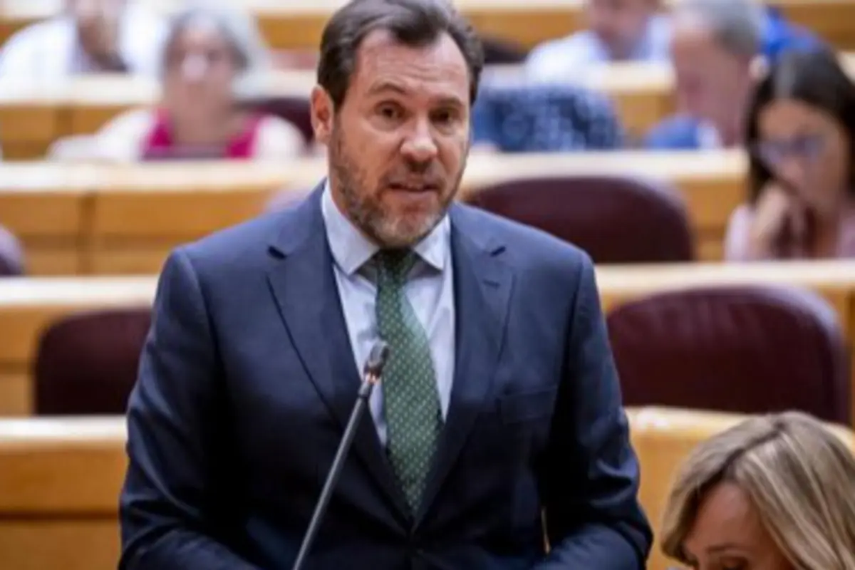 Hombre con traje oscuro y corbata verde hablando frente a un micrófono en un hemiciclo parlamentario Hombre con traje oscuro y corbata verde hablando frente a un micrófono en un hemiciclo parlamentario