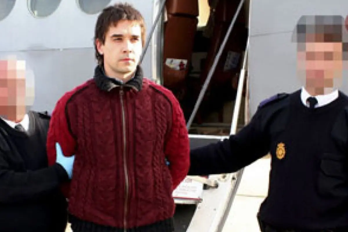 Hombre esposado con chaqueta roja escoltado por dos agentes con el rostro pixelado frente a un avión