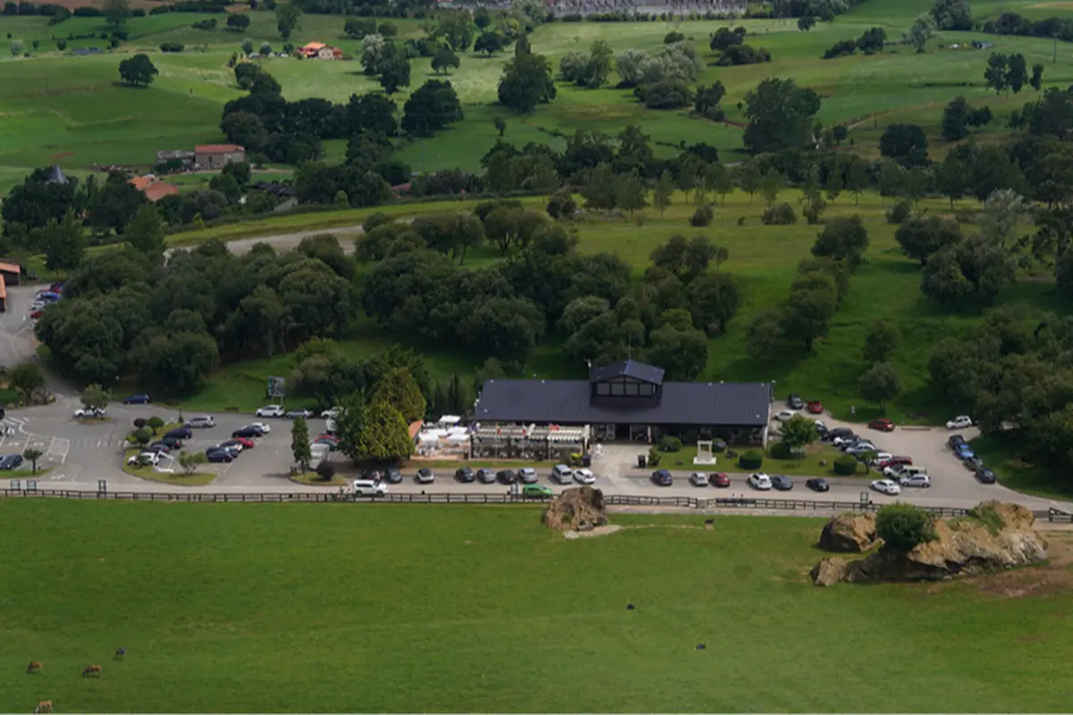 Vista aérea de un edificio con aparcamiento lleno de coches rodeado de prados verdes y árboles en un entorno rural