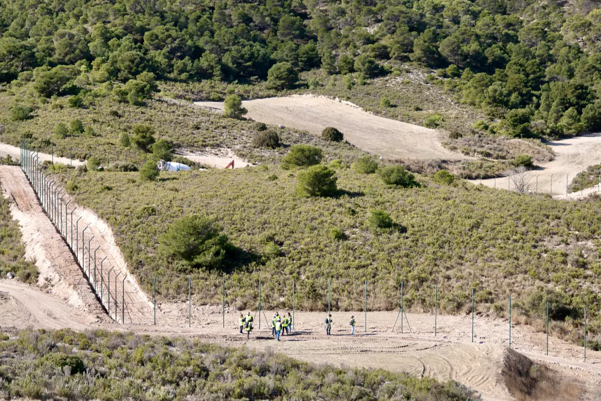 Trabajadores con chalecos reflectantes instalando una valla metálica en una zona rural montañosa cubierta de matorrales y pinos Trabajadores con chalecos reflectantes instalando una valla metálica en una zona rural montañosa cubierta de matorrales y pinos