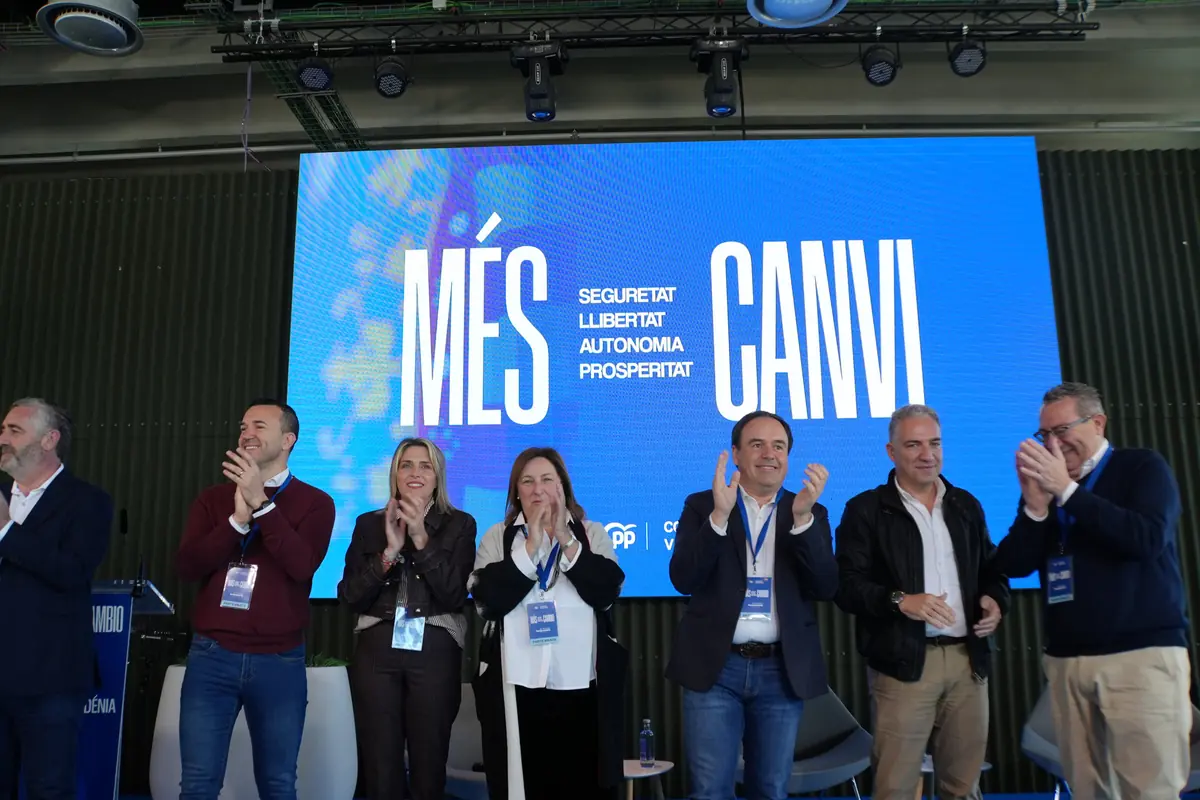 Grupo de personas aplaudiendo en un escenario frente a una gran pantalla azul con el lema en valenciano Més Canvi y palabras como seguretat llibertat autonomia prosperitat