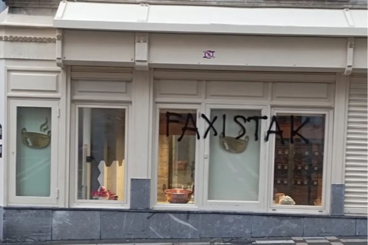 Fachada de una tienda con escaparates blancos y un grafiti negro que dice FAXISTAK sobre los cristales