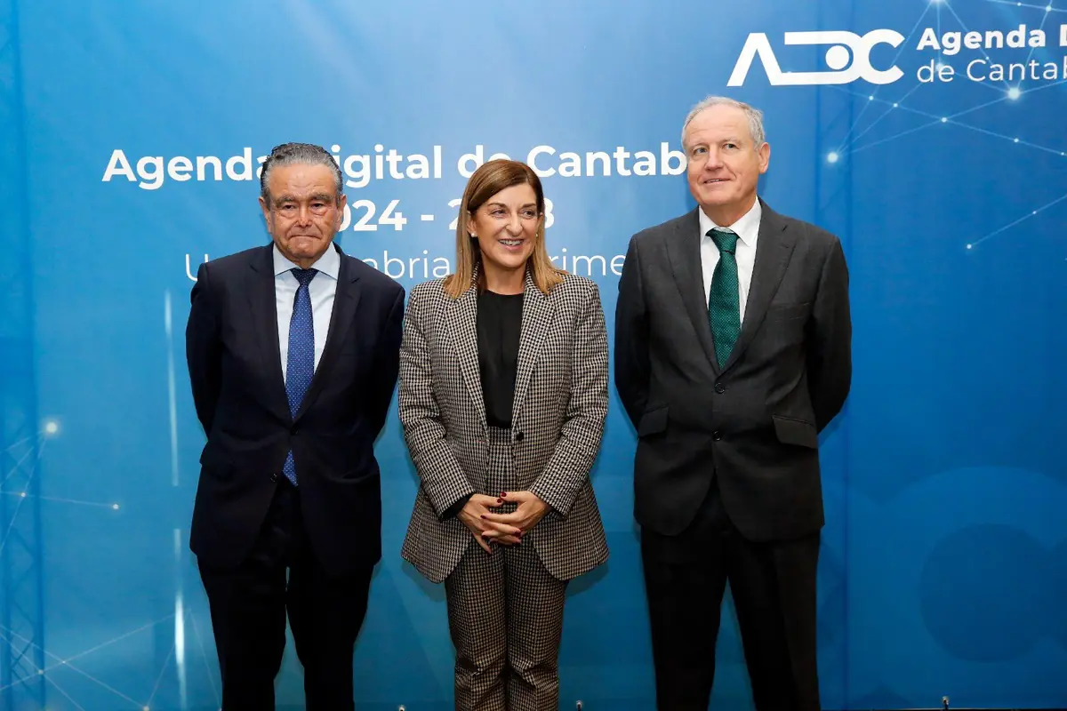 Tres personas con traje posan sonrientes frente a un panel azul de la Agenda Digital de Cantabria