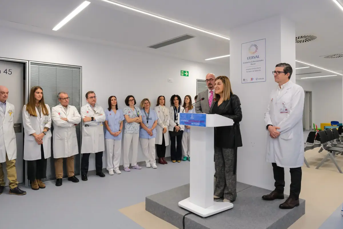 Mujer hablando en un atril durante la inauguración de una unidad hospitalaria rodeada de médicos y personal sanitario con bata blanca y uniforme azul en una sala moderna y luminosa Mujer hablando en un atril durante la inauguración de una unidad hospitalaria rodeada de médicos y personal sanitario con bata blanca y uniforme azul en una sala moderna y luminosa