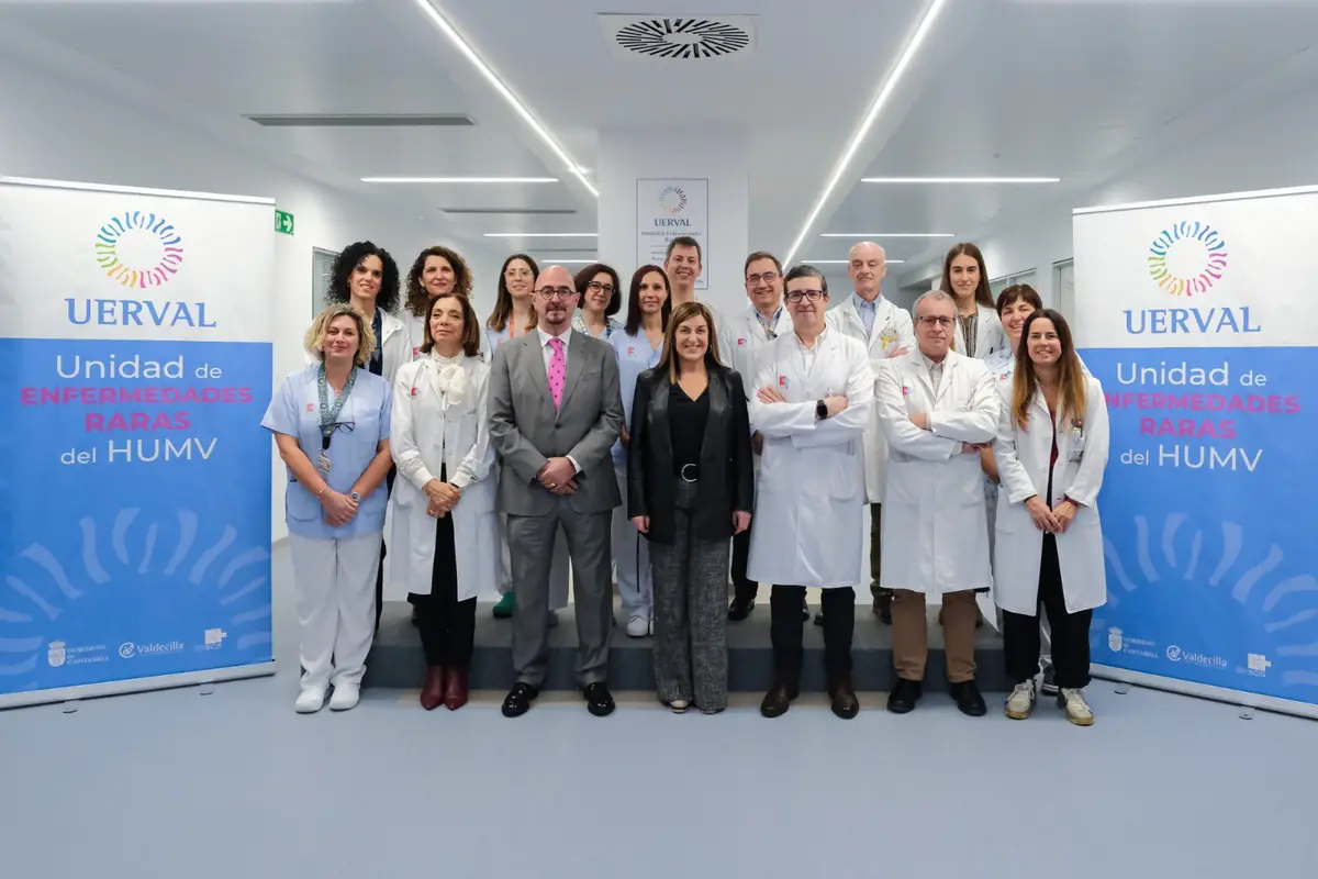 Grupo de profesionales sanitarios y directivos posando en un pasillo hospitalario entre dos lonas de la Unidad de Enfermedades Raras del HUMV Grupo de profesionales sanitarios y directivos posando en un pasillo hospitalario entre dos lonas de la Unidad de Enfermedades Raras del HUMV