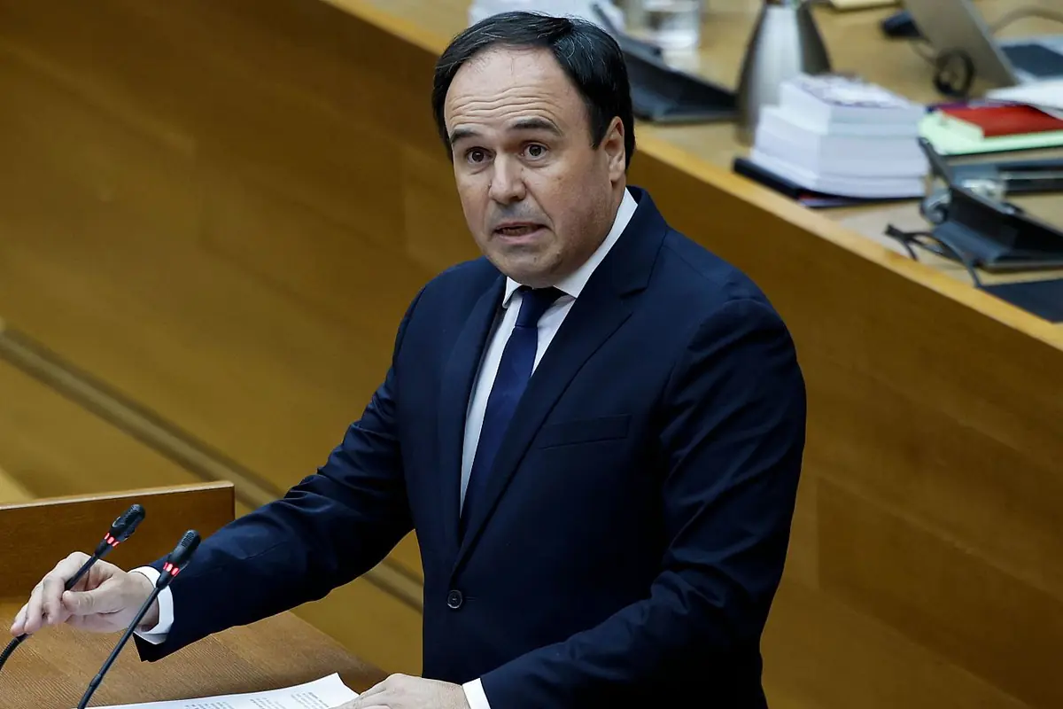 Hombre con traje oscuro hablando en un atril con micrófonos en una sala de plenos o parlamento