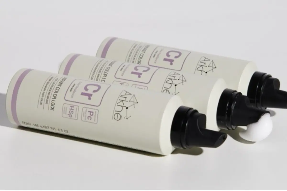 Tres envases de crema capilar marca Arkhé color blanco con detalles en lila colocados en diagonal sobre fondo claro