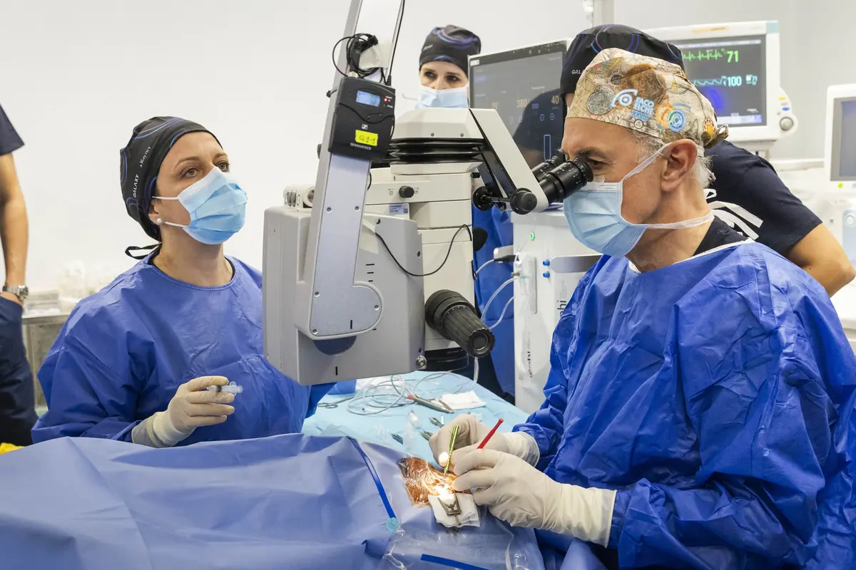 Equipo médico realizando una cirugía ocular con microscopio en un quirófano moderno mientras varios profesionales observan y asisten al cirujano principal