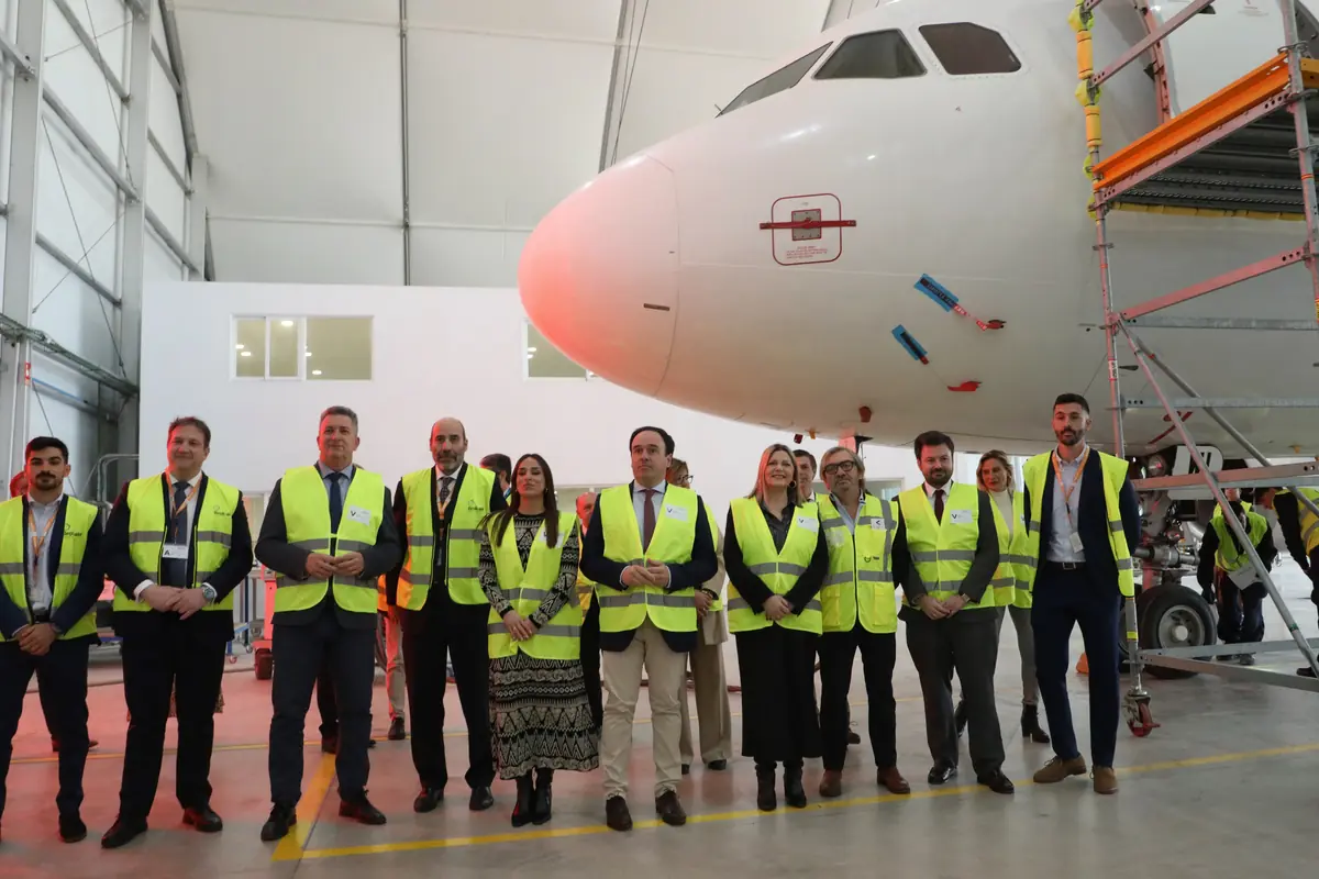 Grupo de personas con chalecos reflectantes posando frente al morro de un avión dentro de un hangar de mantenimiento