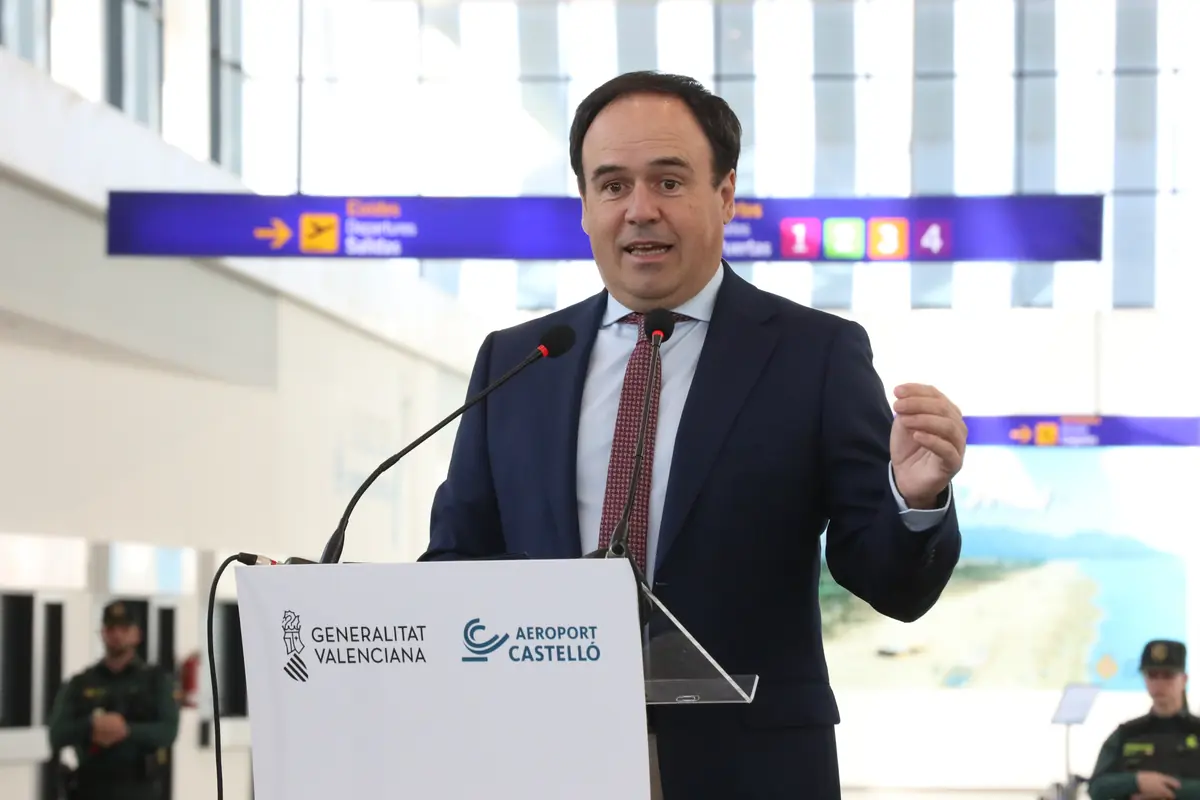Hombre con traje hablando en un atril del Aeropuerto de Castellón dentro de una terminal con carteles de salidas al fondo