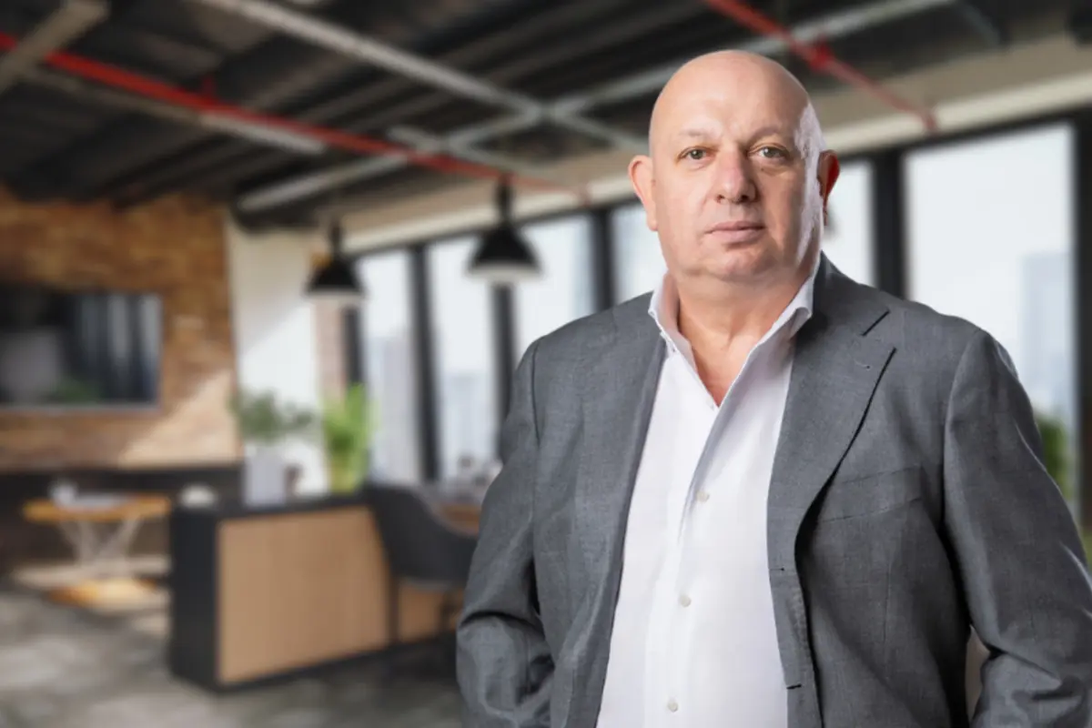 Hombre calvo de mediana edad con traje gris y camisa blanca posando en una oficina moderna desenfocada de fondo
