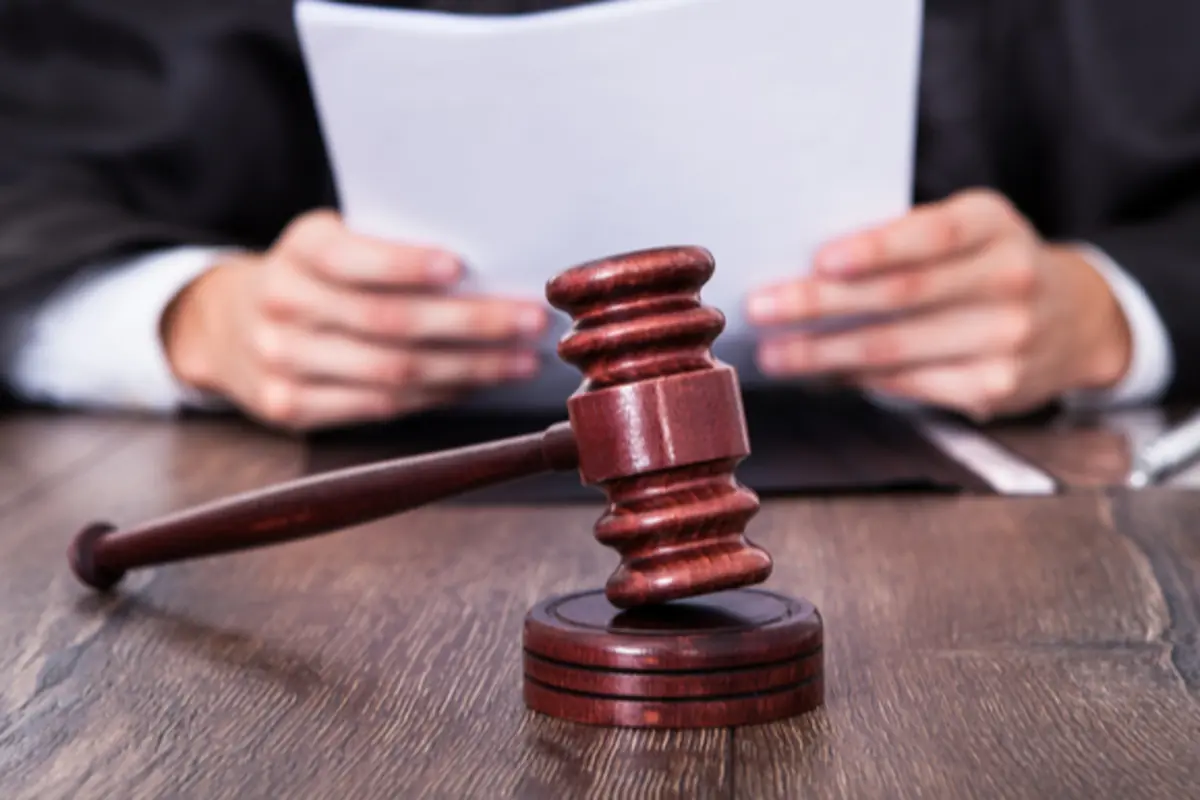 Mazo de juez de madera sobre una mesa con una persona leyendo documentos al fondo
