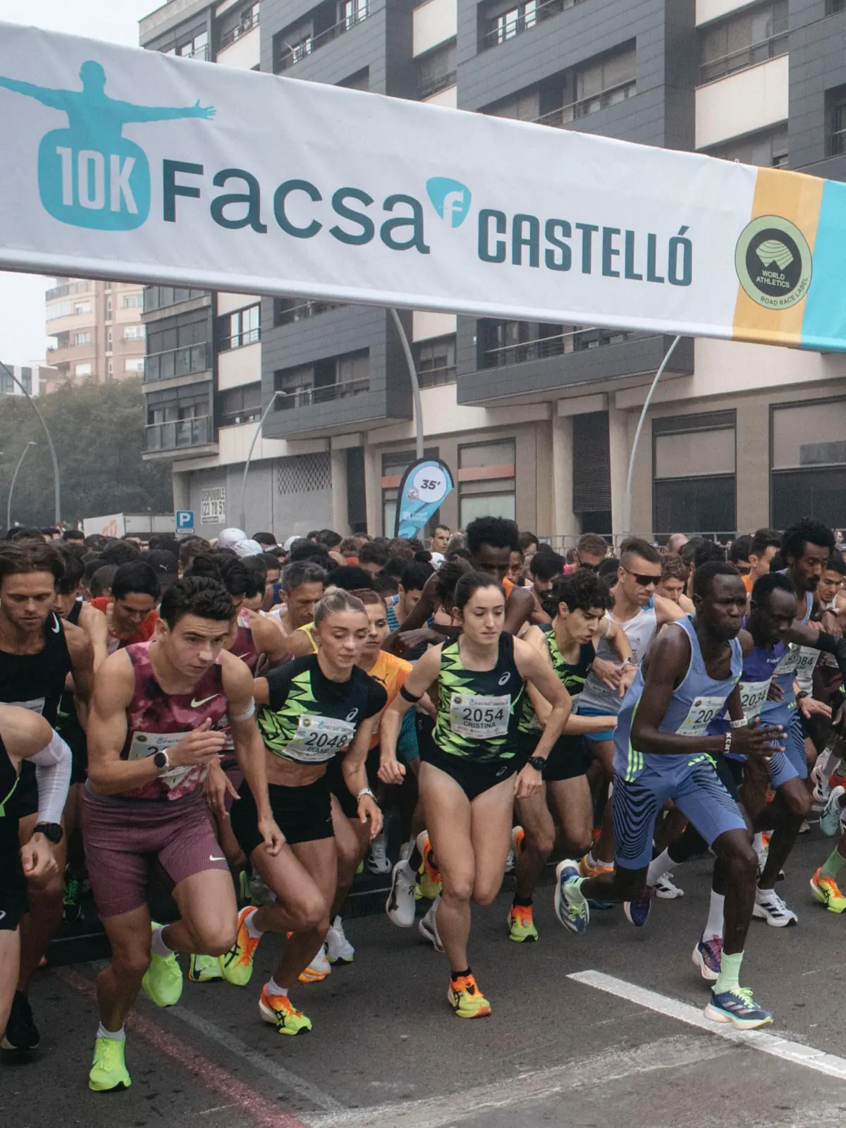 Salida masiva de corredores al inicio de una carrera urbana de 10K en Castellón bajo un gran arco publicitario Salida masiva de corredores al inicio de una carrera urbana de 10K en Castellón bajo un gran arco publicitario