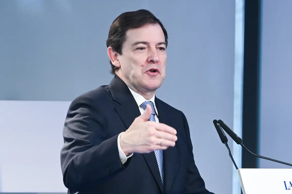 Hombre de mediana edad con traje oscuro hablando en un podio y gesticulando con la mano frente a dos micrófonos Hombre de mediana edad con traje oscuro hablando en un podio y gesticulando con la mano frente a dos micrófonos