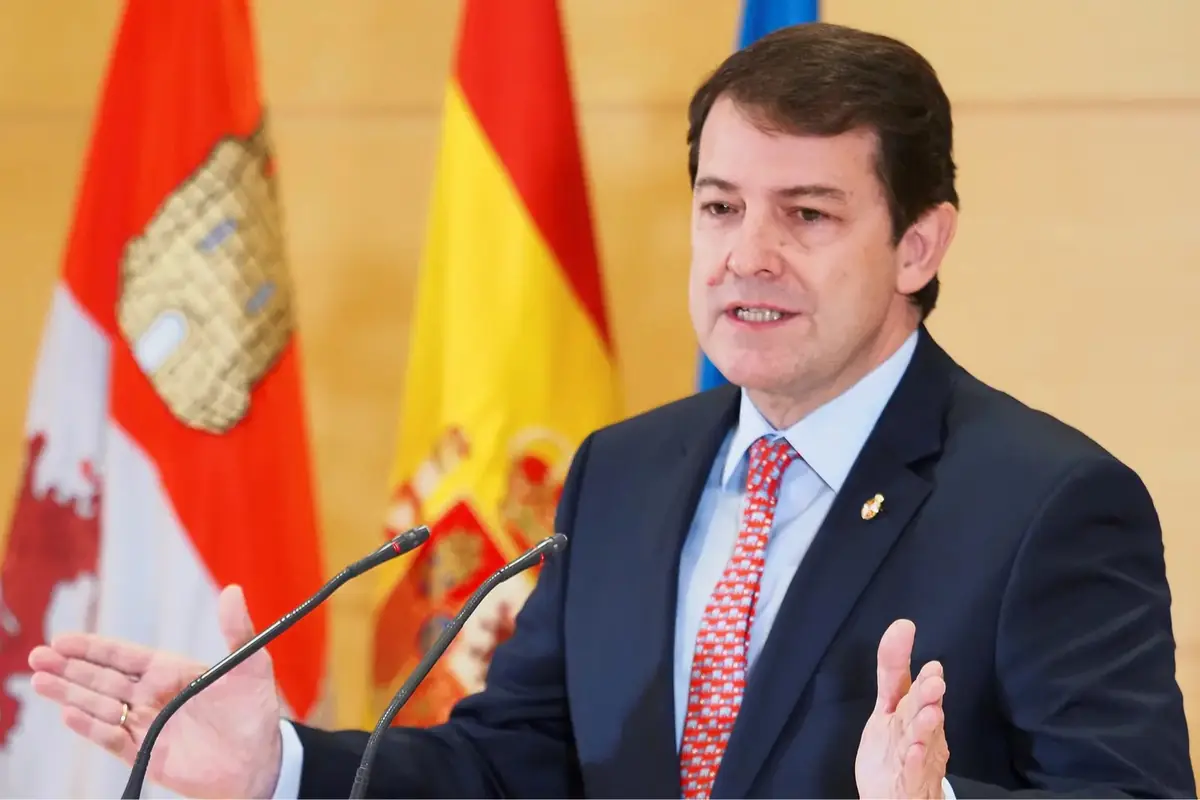 Hombre con traje y corbata roja hablando en un atril con micrófonos frente a banderas de España y de una comunidad autónoma