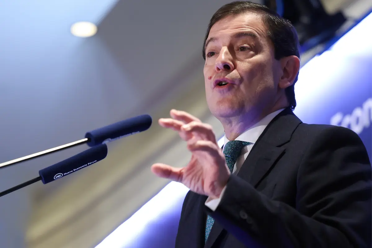 Hombre con traje y corbata hablando en un podio frente a dos micrófonos azules