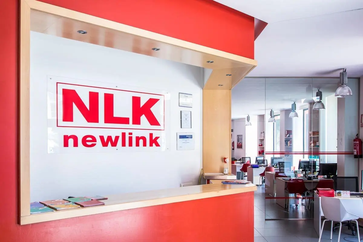 Recepción de la academia NLK Newlink con mostrador rojo, logotipo en la pared y vista de una oficina moderna con varios puestos de trabajo al fondo