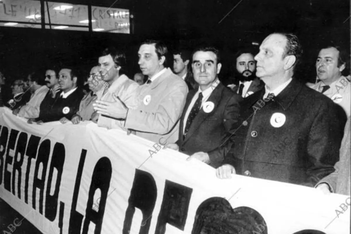 Manifestación en blanco y negro con un grupo de hombres trajeados sosteniendo una gran pancarta con la palabra libertad visible en primer plano