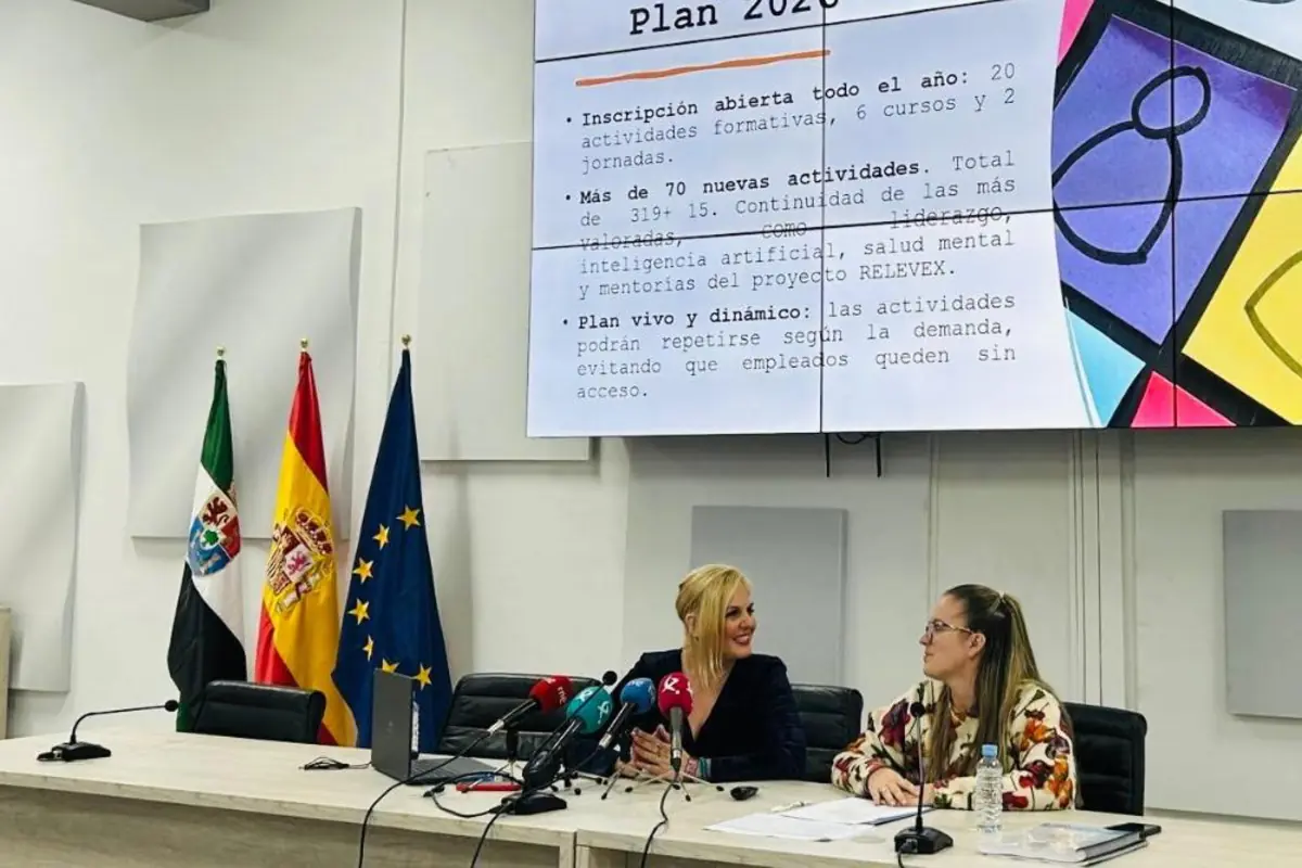Dos mujeres sentadas en una mesa de conferencias con micrófonos frente a ellas mientras presentan un plan de formación proyectado en una gran pantalla junto a las banderas de Extremadura España y la Unión Europea