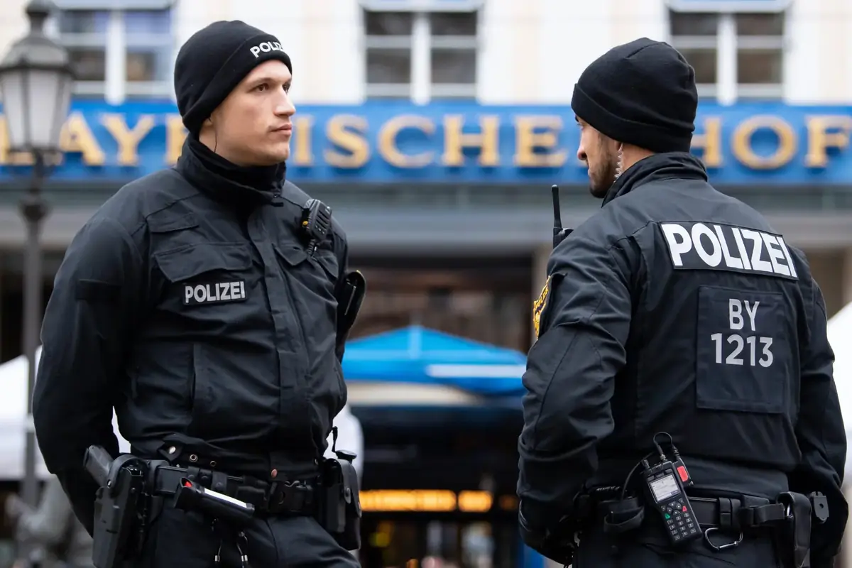 Dos agentes de policía alemana con uniforme negro conversan en la calle frente a un edificio urbano