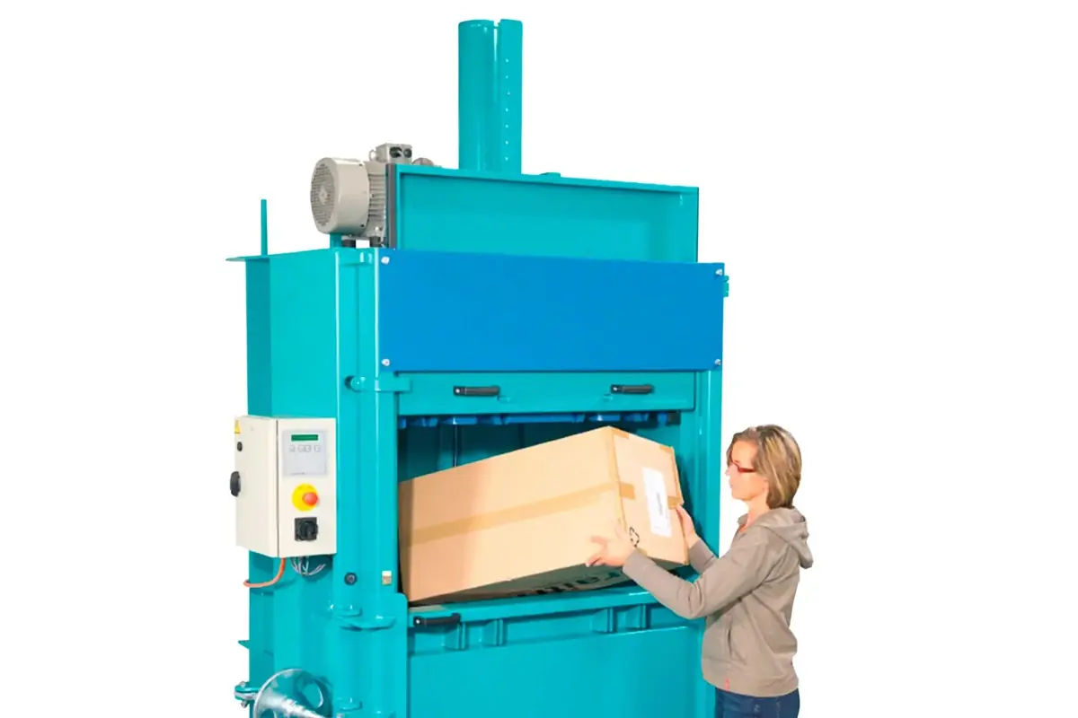 Mujer introduciendo una caja de cartón grande en una prensa compactadora industrial azul