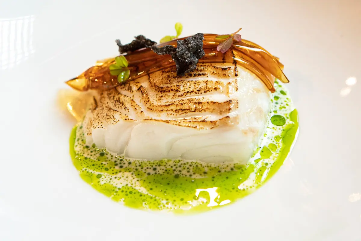 Lomo de pescado blanco a la plancha servido sobre salsa verde espumosa con crujientes decorativos y brotes frescos