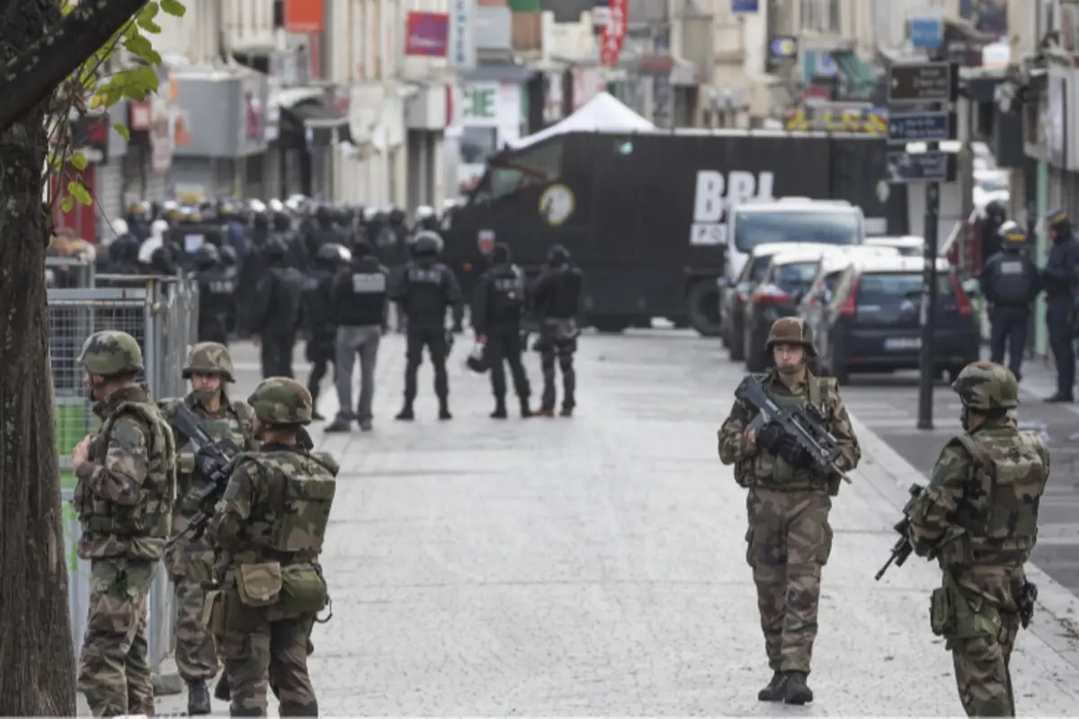 Soldados y policías fuertemente armados controlan una calle urbana acordonada con vehículos oficiales al fondo durante un operativo de seguridad