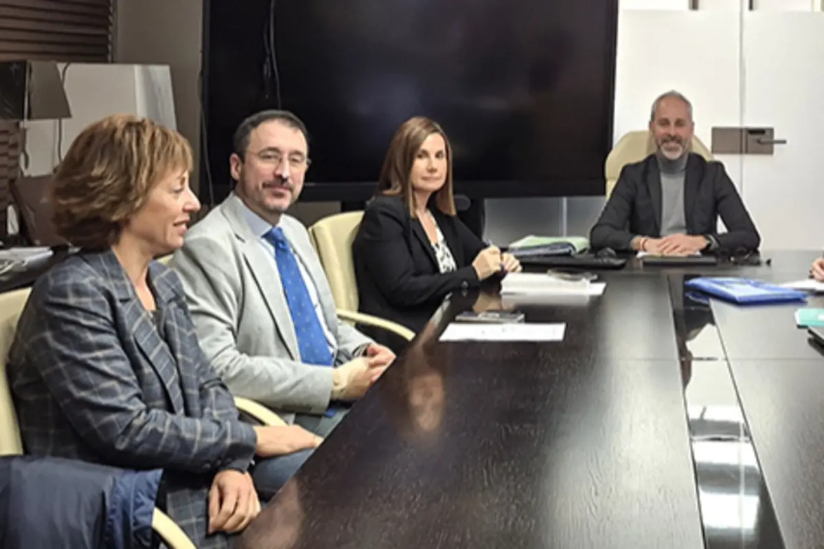 Cuatro personas sentadas alrededor de una mesa de reuniones en una sala de conferencias con documentos y una gran pantalla al fondo