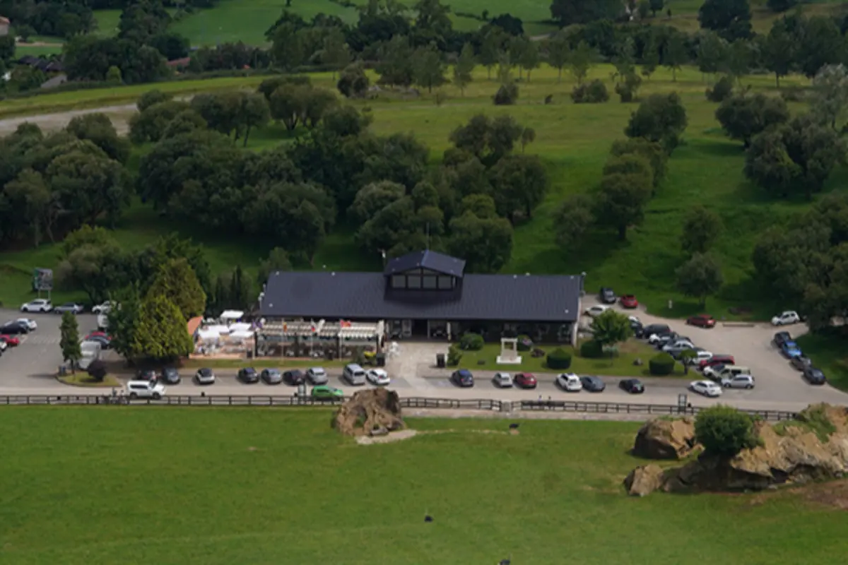 Vista aérea de un edificio con aparcamiento lleno de coches rodeado de prados verdes y árboles